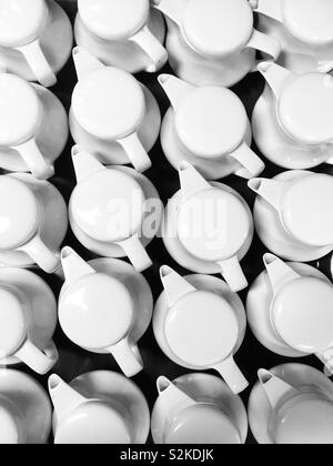 Group of white tea pots in rows from above. Shapes and patterns form, looking down on multiple white teapots on black table, restaurant or cafe background. Stock Photo