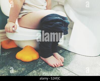 Lower half of toddler girl sitting on a potty beside a toilet in a bathroom Stock Photo