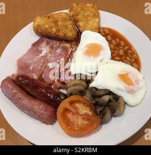 Gourmet English cooked breakfast of bacon, fried eggs, baked beans, mushrooms, sausages, tomato and hash browns. This popular breakfast meal has regional variants and is often accompanied by toast. Stock Photo