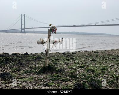 A wooden cross sits in mud on the north bank of the River Humber as a memorial to past tragic events that have occurred on the river. At high tide the cross is covered and revealed again at low tide. Stock Photo