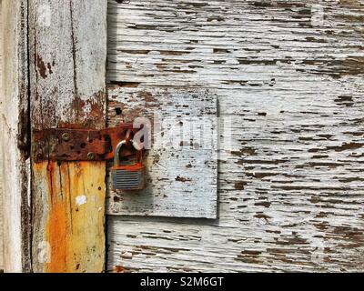 Rusted padlock on an old wooden door with flaking white paint. Stock Photo