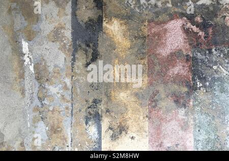 Detail of rough concrete texture with partial remains of red, yellow, and black colored flooring creating a grunge pattern Stock Photo
