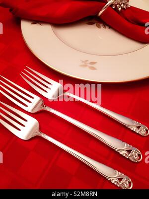 Formal table setting with silver forks fine China and cloth napkins on a red tablecloth Stock Photo