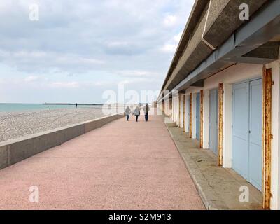 Three persons walking past pastel coloured beach cabins on the Dieppe waterfront off season. Stock Photo