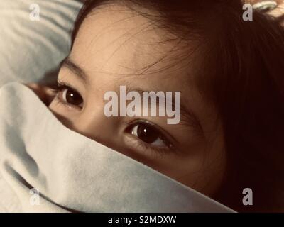 Closeup of a young girl’s dark brown eyes.  A summer cotton bed sheet is covering her mouth and nose. Stock Photo