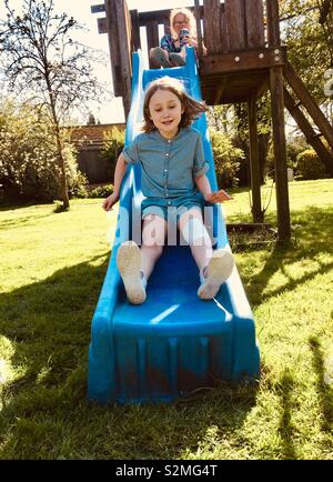 Sisters playing on a slide in garden Stock Photo