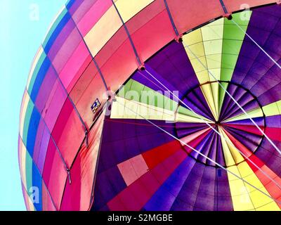 View from underneath of colourful rainbow hot air balloon against blue sky Stock Photo