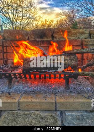 Outdoor fireplace with a huge log and a roaring fire. Stock Photo