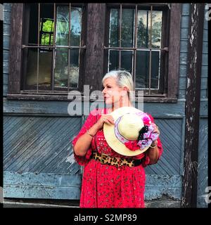 Woman standing in front of train depot wearing a red dress and holding a hat Stock Photo