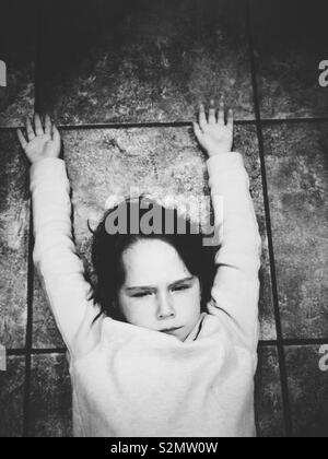 Angry young girl laying on tile floor with arms up Stock Photo
