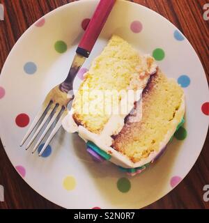 A slice of sponge cake with butter icing and jam filling on a spotty plate with a fork. Stock Photo