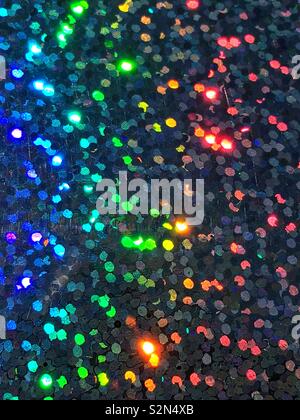 Bright blue, yellow, orange, and green colorful holographic, abstract, and prismatic arrangement of small tiny sequins  reflecting in the light. Stock Photo