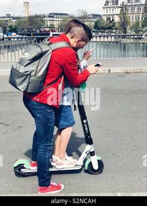 Young fashionable couple trying to figure out an electric Lime scooter on a bridge in Paris Stock Photo