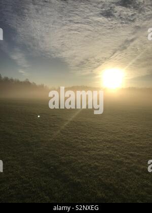 Early misty morning with Sun rising over the fields Stock Photo