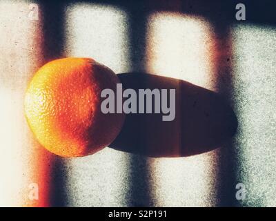 Orange in sunlight with shadows from window blinds Stock Photo