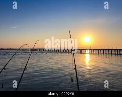 Lines set for early morning fishing trip with lone walker on pier in the background just after sunrise at Rye Victoria Australia Stock Photo
