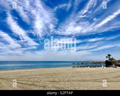 A beach scene in Torrox, Costa del Sol, Spain showing deep blue sky, golden sands and blue sea. Beach shades are in the middle distance. Stock Photo