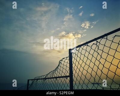 Broken chicken wire fence on the beach at sunrise Stock Photo
