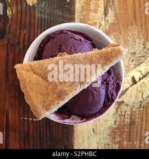 Blueberry ice cream in white cup with cookie on top, seen from above on wooden table Stock Photo
