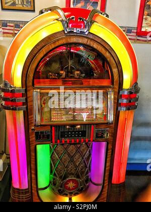An old fashioned neon pink green orange and yellow nickelodeon aka jukebox sitting in old fashioned diner Stock Photo