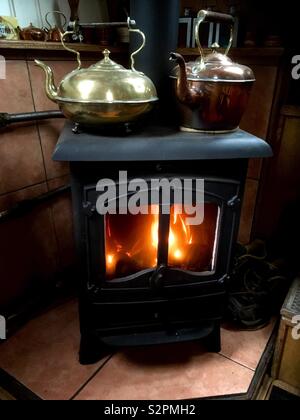Cast iron black stove with a brass and a copper kettle on the top warming from the flames of a warm fire in the stove. Stock Photo