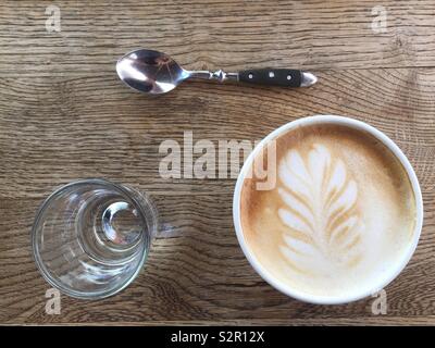 Cappuccino coffee, a glass of water and a teaspoon on a wooden table Stock Photo