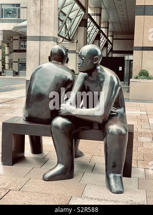 London, UK - 15th June 2019: Bronze sculpture Two Men on a Bench by Giles Penny, (1995). Canary Wharf. Stock Photo