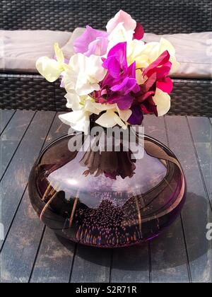 Bunch of sweet peas in a purple, glass vase on an outdoor table Stock Photo