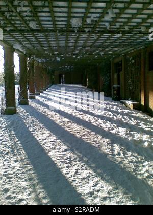 The afternoon sun casts dramatic shadows onto the snow in the pergola in Valley Gardens Harrogate Stock Photo