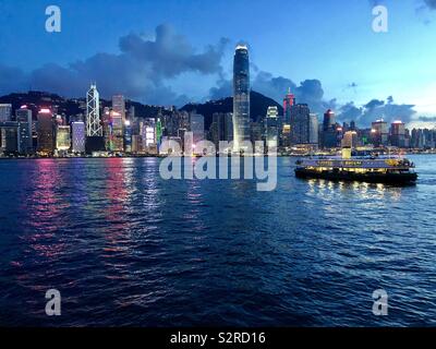 HONG KONG -29 JUN 2019- Night view of colored neon lights on tall buildings on the Hong Kong skyline with boats crossing Victoria Harbour. Stock Photo