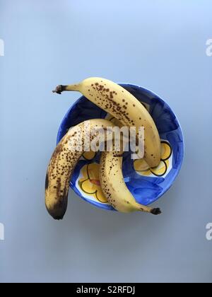 Three ripe bananas in a blue and yellow bowl on a light surface Stock Photo