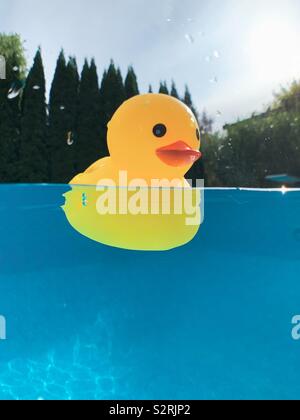 Yellow toy rubber duck floating on water in an outdoor swimming pool with over under water perspective. Stock Photo