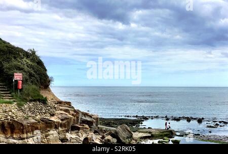 Father and daughter studying rock pools at a peaceful seaside inlet at Scalby Mills near Scarborough, North Yorkshire, UK. This place is near Scalby Ness Rocks and the North Bay beach. Stock Photo