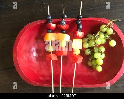 A red platter tray of fruit skewers on a wooden table top. Stock Photo