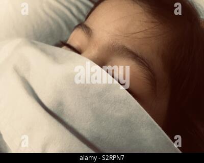 A closeup view of a summer cotton bed sheet covering a young multi-ethnic girl’s mouth and nose. Stock Photo