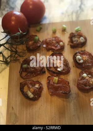Roasted red tomatoes with chopped onions and garlic seasoning on display on the wooden cutting board in the kitchen Stock Photo