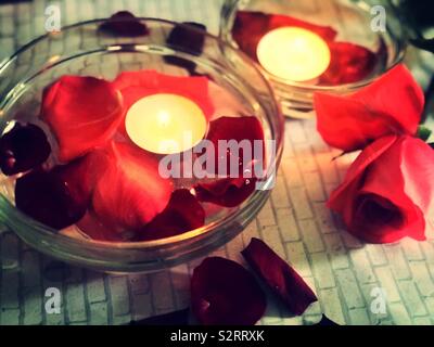 A beautiful ambiance of tea light candles floating in the water with soft red flower petals , roses