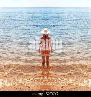 Woman standing in the shallows looking out at the ocean Stock Photo