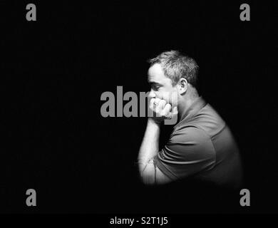 Man thinking with face resting on hand in darkness Stock Photo