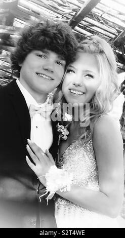 Young couple at Prom. Beautiful blonde hair girl with wavy hair, handsome brown hair boy. Smiling showing teeth. Sunlight shining on them in a rustic setting Stock Photo