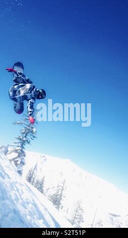 Bear Valley Ski Resort, Northern California. A snowboarder in the air doing a trick . Beautiful blue sky. Wearing red gloves and black and white jacket. Trees with snow in the background. Stock Photo