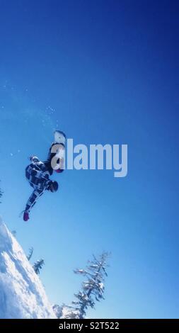 Bear Valley Ski Resort, Northern California. A snowboarder in the air doing a trick. Trees with snow in the background. Black and white jacket. Stock Photo