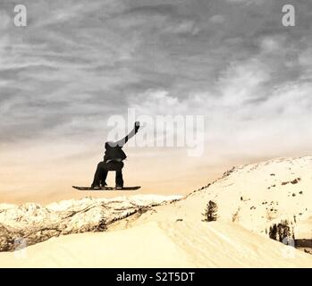 Bear Valley Ski Resort, Northern California. A snowboarder in the air doing a trick, grabbing his board one arm in air. Trees with snow in the background. Stock Photo