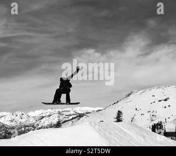 Bear Valley Ski Resort, Northern California. A snowboarder in the air doing a trick, grabbing his board one arm in air. Trees with snow in the background. Black and white picture. Stock Photo