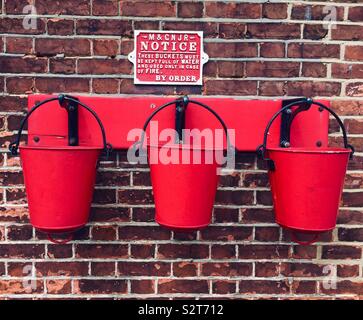 Three vibrant red Fire buckets hanging on a wall Sheringham station Stock Photo