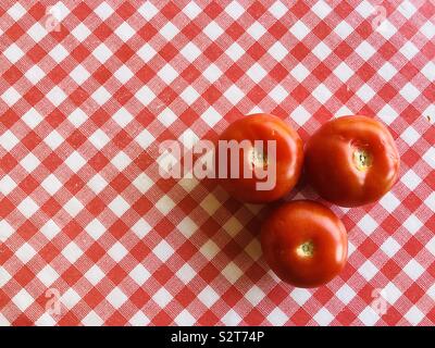 Three large tomatoes on red and white checked background Stock Photo