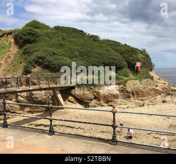 Father and daughter studying rocks and pools at a peaceful seaside inlet at Scalby Mills near Scarborough, North Yorkshire, UK. This is near Scalby Ness Rocks and the North Bay beach. Stock Photo