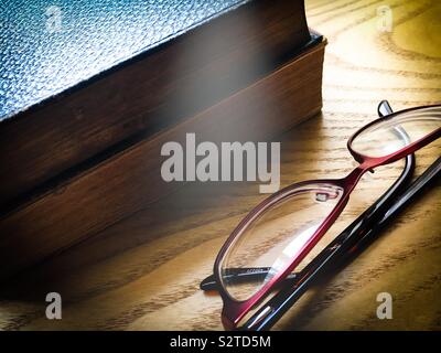 Two old vintage books and a pair of reading glasses laid on a wooden table Stock Photo