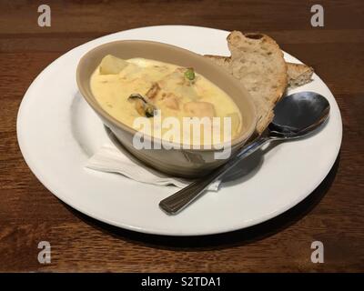 Cullen skink traditional Scottish soup is shown, containing white fish, potatoes, onions, milk, and, in this version, mussels. Bread is served on the side. Stock Photo