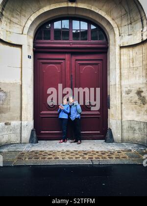 Middle aged couple looking at their phones next to an old door in Paris Stock Photo